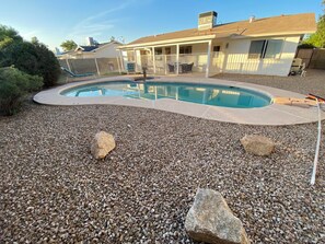 A swimming pool with a pebble surround, a covered patio, and a house in the background. - Mesa Nomad Mecca refreshing Diving Pool + splash pad & patio, Dog friendly! (Mesa)