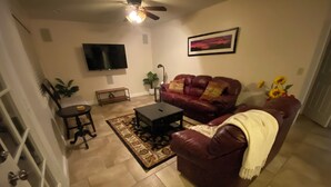 A living room with a leather sofa, a coffee table, a TV, and a painting on the wall. - Mesa Nomad Mecca refreshing Diving Pool + splash pad & patio, Dog friendly! (Mesa)