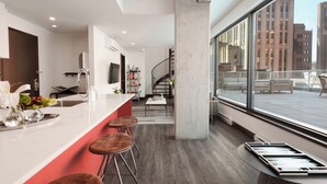 A modern kitchen with a bar area, a staircase, and a view of the city through large windows. - Penthouse | Luxury Residence Old Montreal, Private Terrace, Two Levels (Montréal)