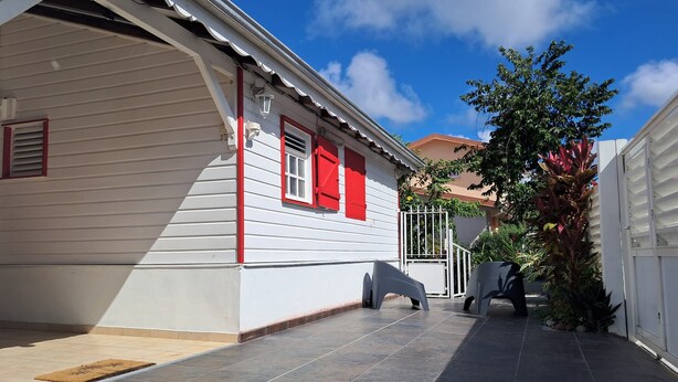 A white building with red shutters, a tiled patio, and a gated entrance. - BlueHorizon180 is located in Ducos, the central town of Martinique. (Ducos)