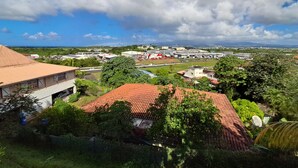 A residential area with houses, a road, and a distant view of a commercial area with buildings and a gas station. - BlueHorizon180 is located in Ducos, the central town of Martinique. (Ducos)