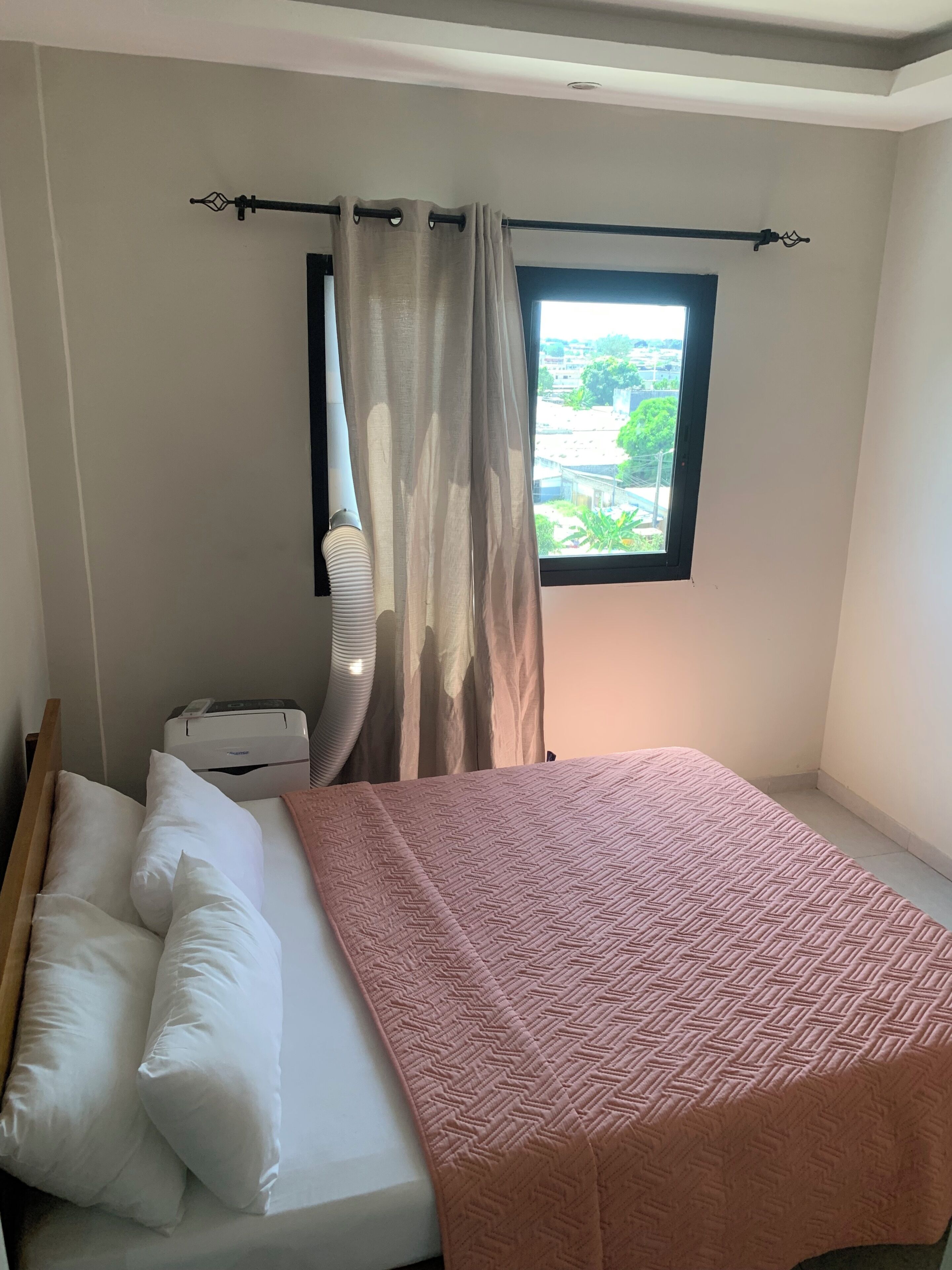 Une chambre à coucher avec un lit, des oreillers, un radiateur, une fenêtre donnant sur un beau paysage et un rideau.