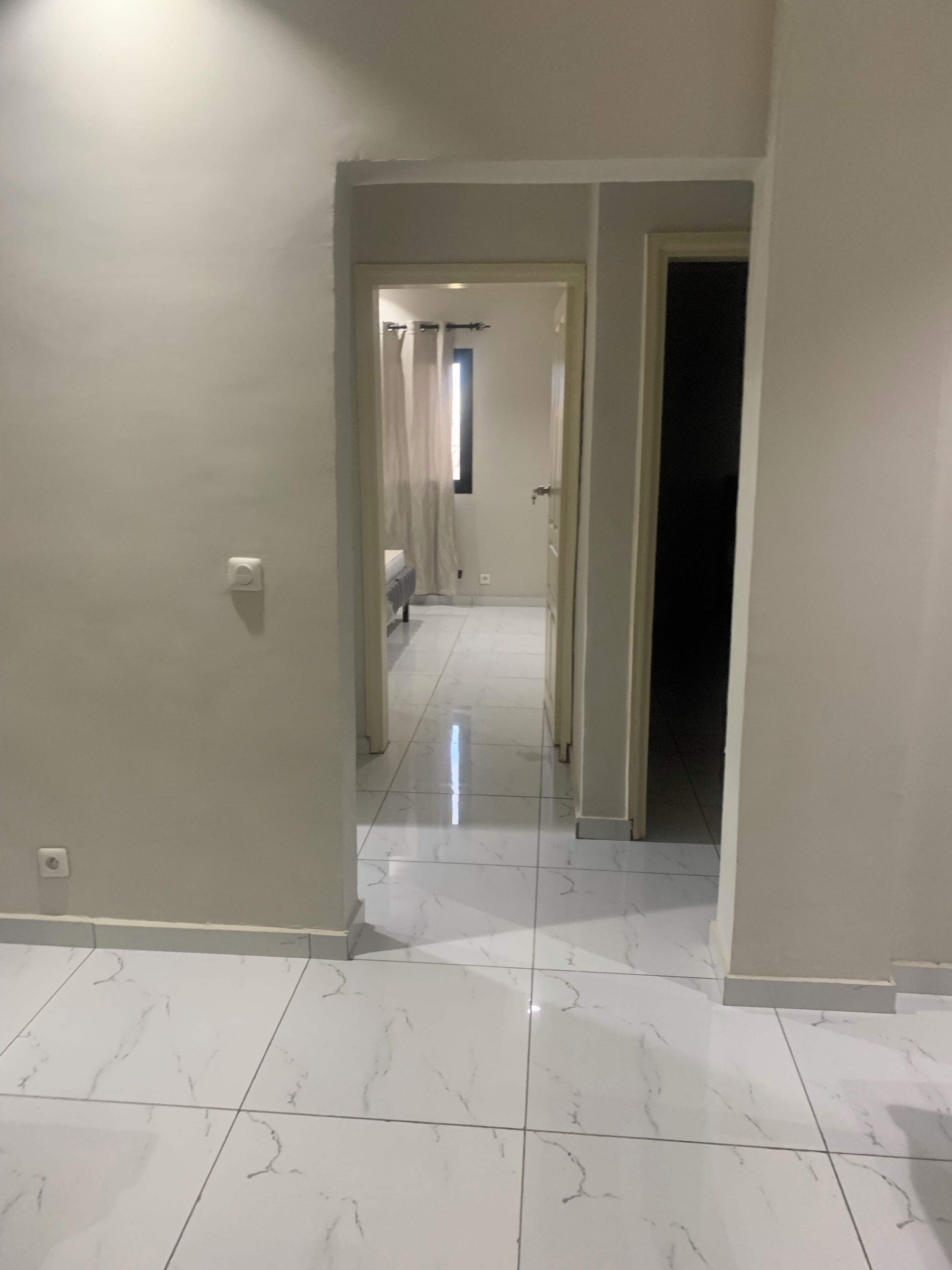 A hallway with a tiled floor, a door at the end, and a light fixture on the wall.
