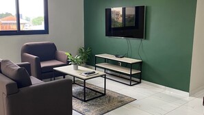 Una sala de estar con un sofá, una mesa de centro, televisor y una planta.