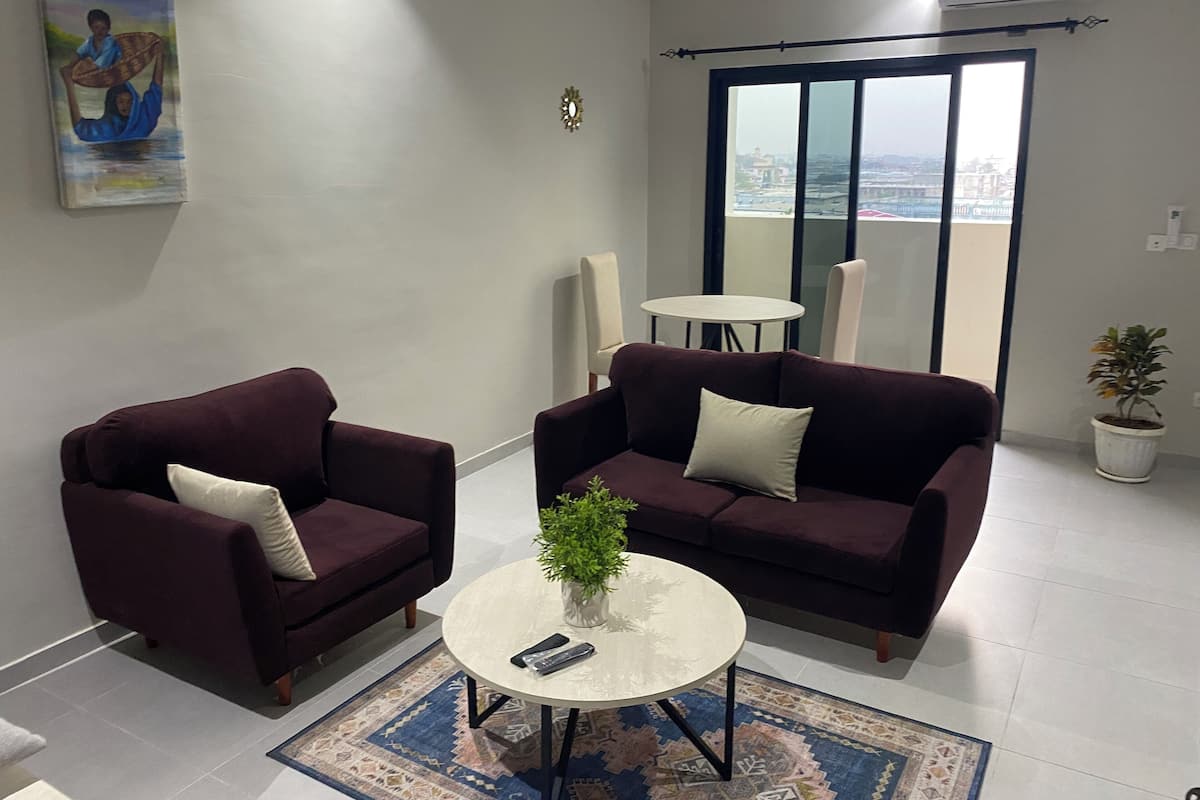 Una sala de estar con dos sofás oscuros, una pequeña mesa redonda de centro, una planta en maceta y un cuadro en la pared.