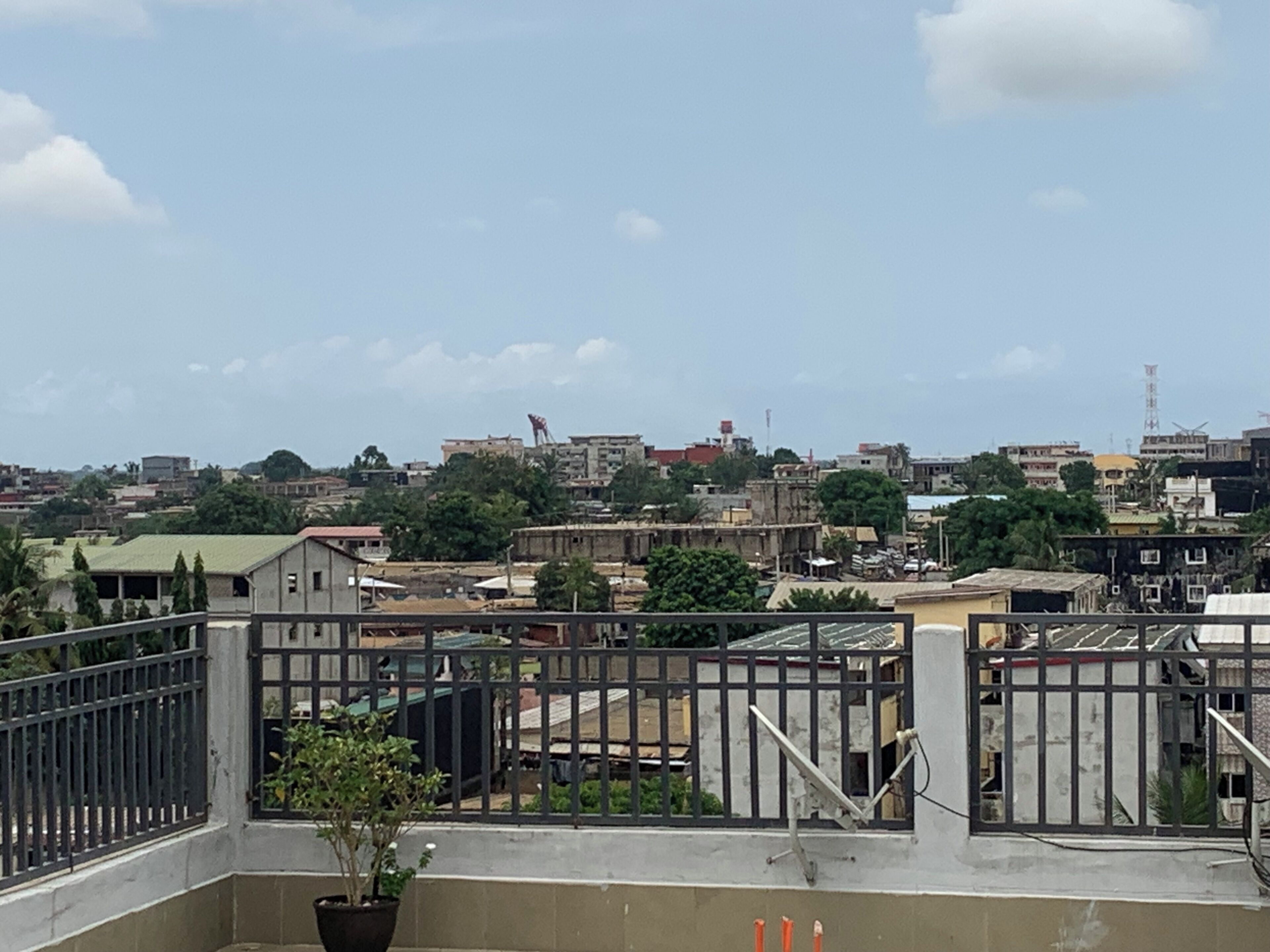 A cityscape with buildings, a satellite dish, and a potted plant on a balcony.