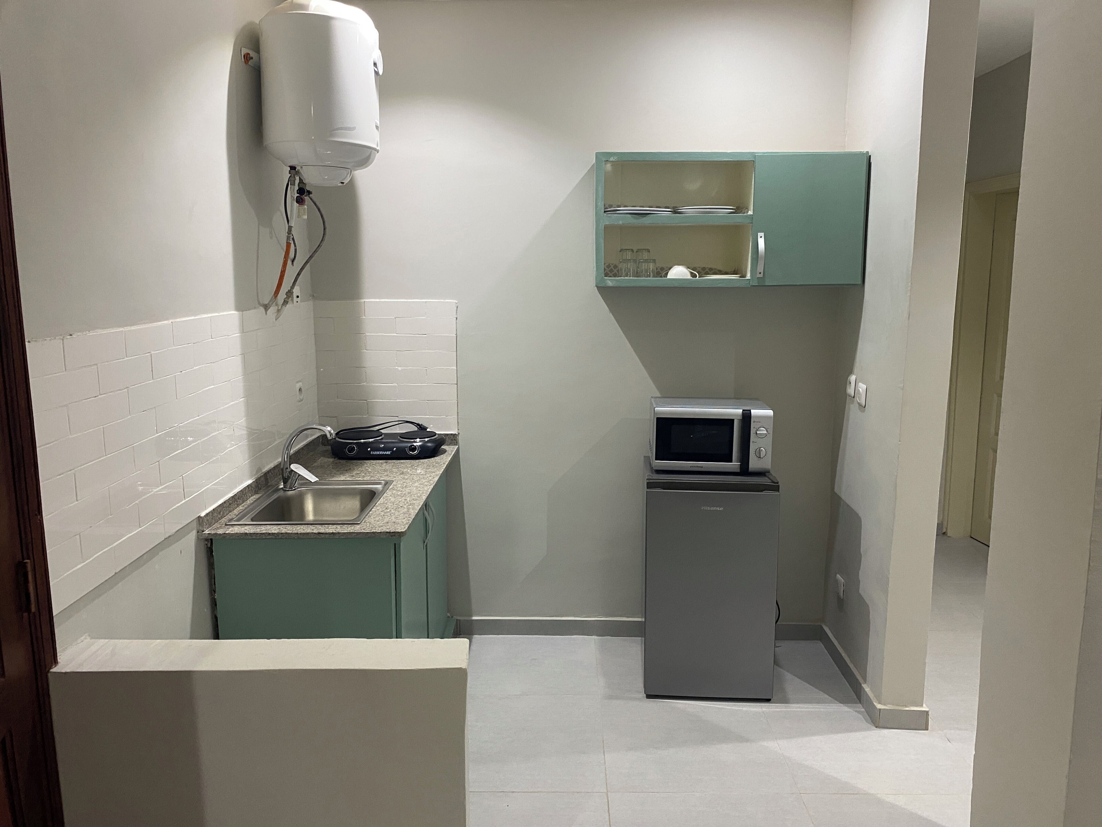 Una cocina compacta con microondas, un refrigerador pequeño, un lavamanos y un calentador de agua.