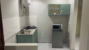 Una cocina compacta con microondas, un refrigerador pequeño, un lavamanos y un calentador de agua.