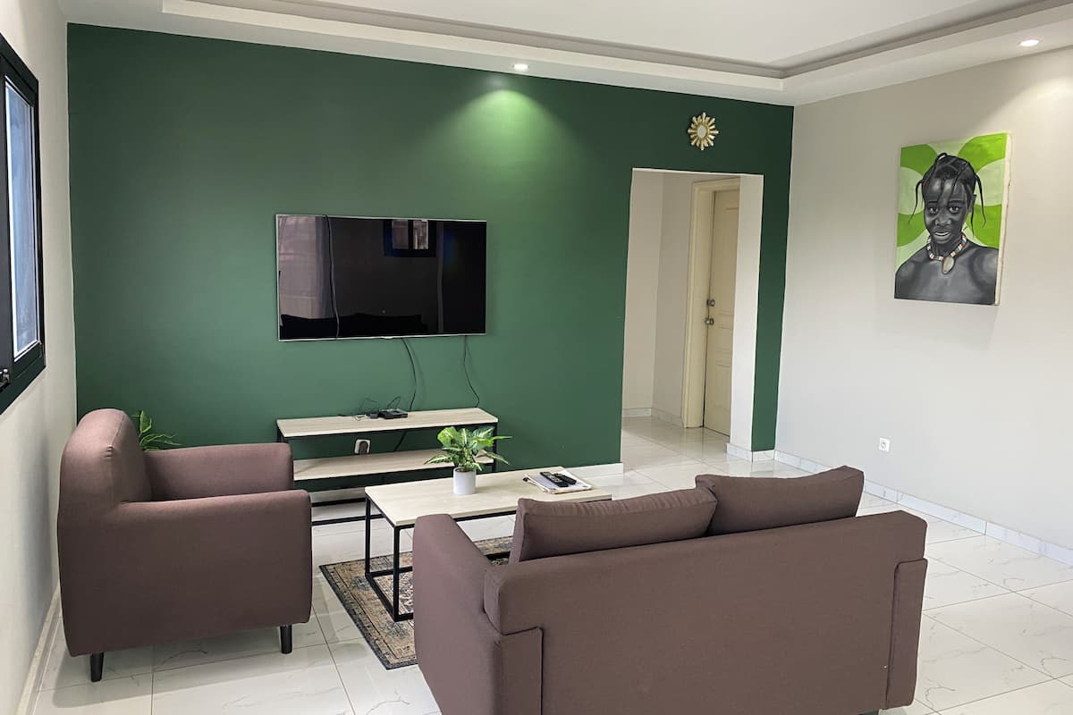 Una sala de estar moderna con una pared de acento verde, un televisor de pantalla plana, un sofá, una mesa de centro y un cuadro.