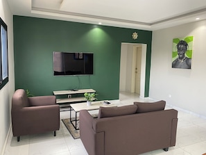 A modern living room with a green accent wall, a flat-screen TV, a sofa, a coffee table, and a painting.