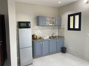 A compact kitchen with a refrigerator, microwave, sink, and cabinets.