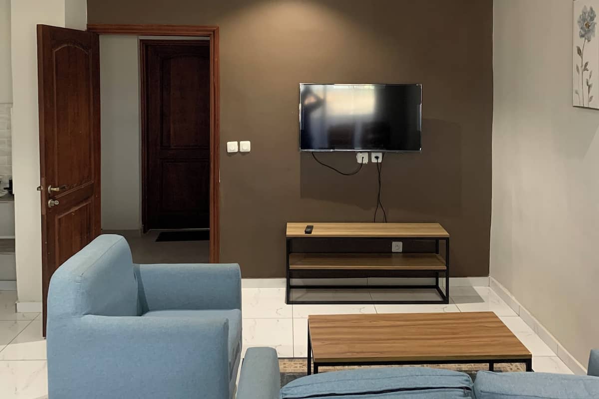 Una sala de estar con un sofá, una mesa de centro, un televisor montado en la pared y una puerta de madera.