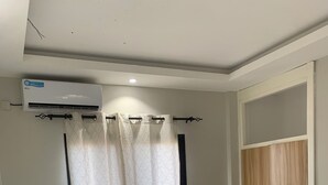 Un dormitorio con cama, lámpara de noche, ventana con cortinas, aire acondicionado y armario.