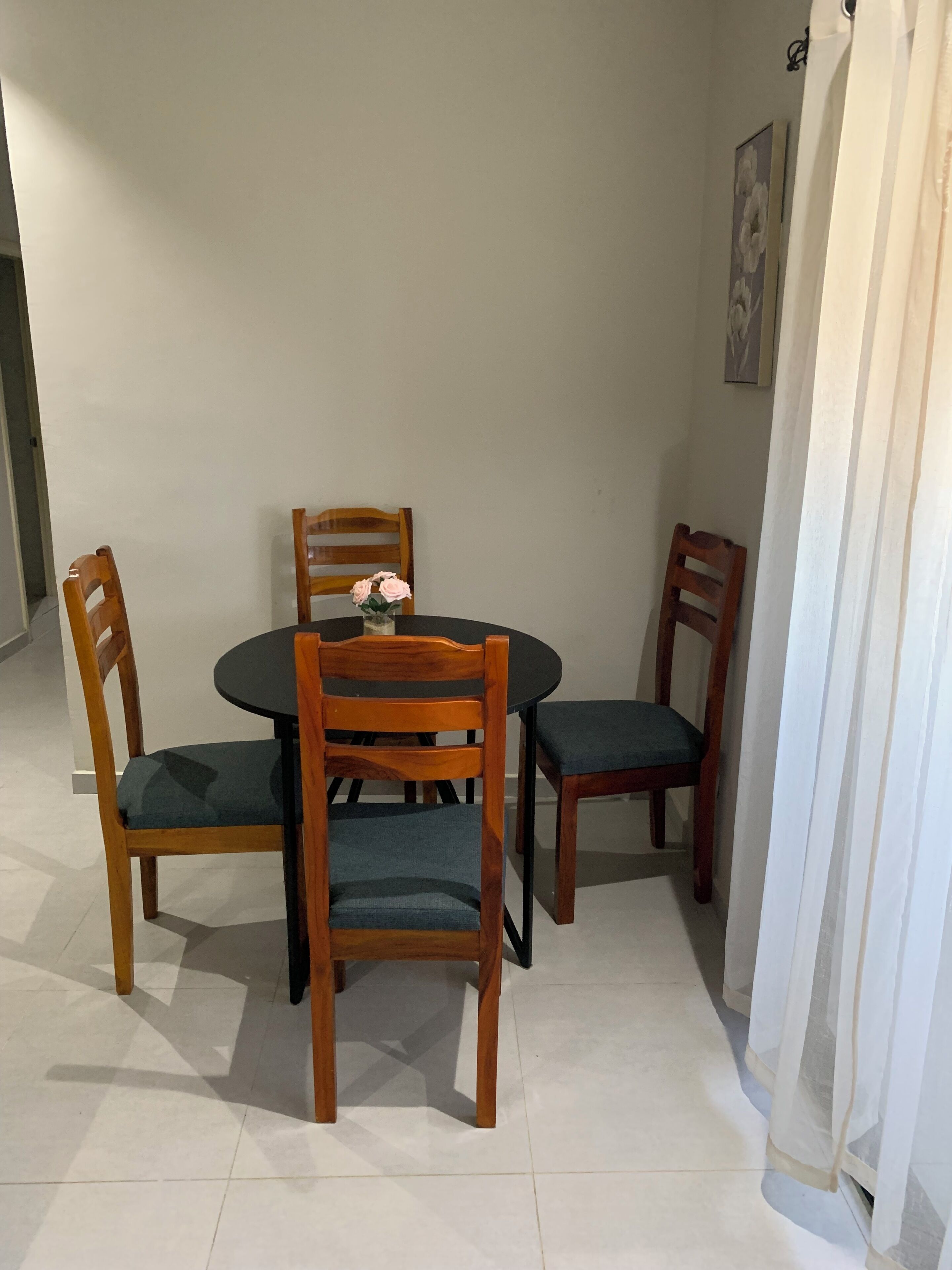 Un comedor con una mesa redonda, cuatro sillas de madera y un florero con flores.