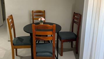 Un comedor con una mesa redonda, cuatro sillas de madera y un florero con flores.