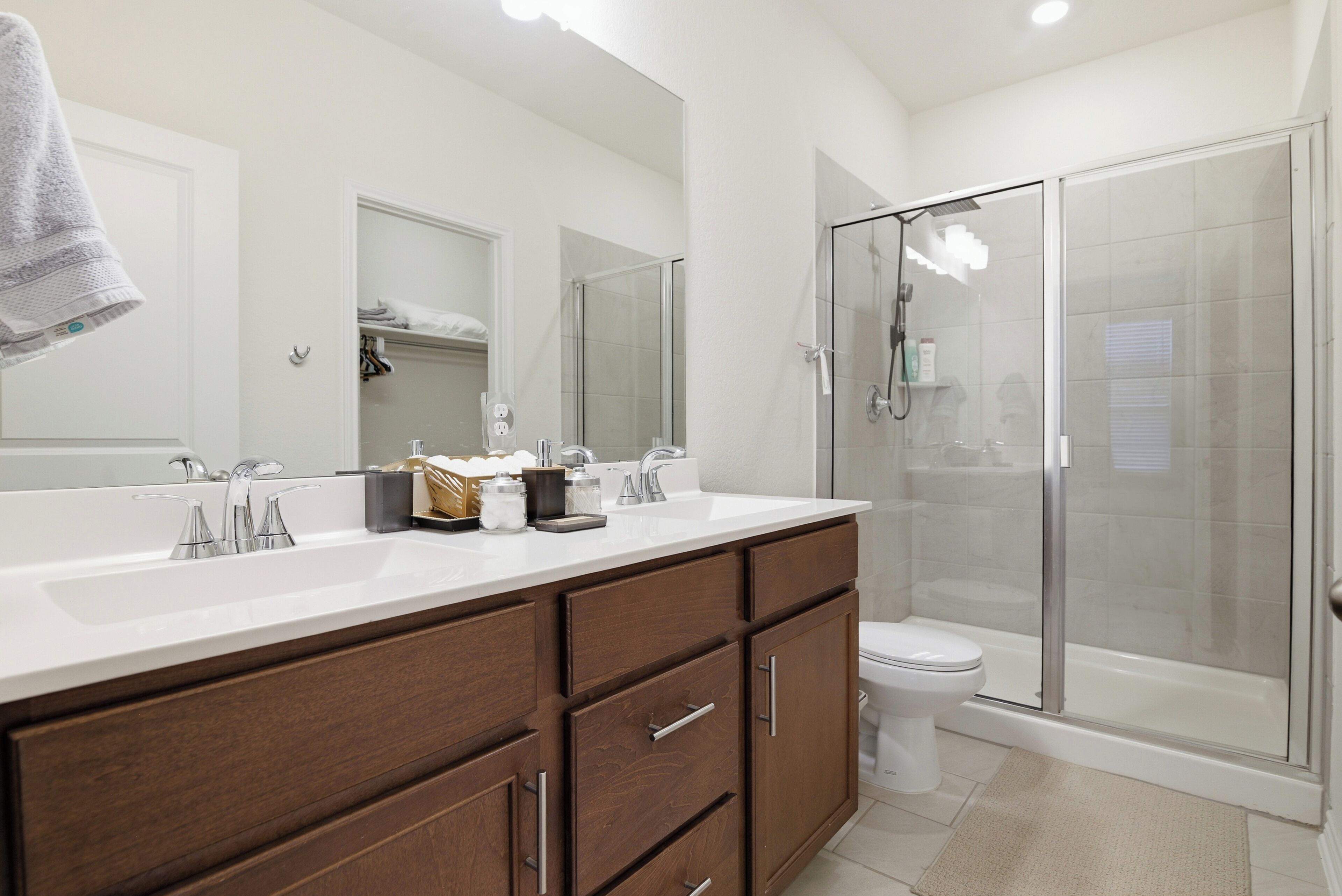 A modern bathroom with a large mirror, dual sinks, a shower enclosure, and a toilet.