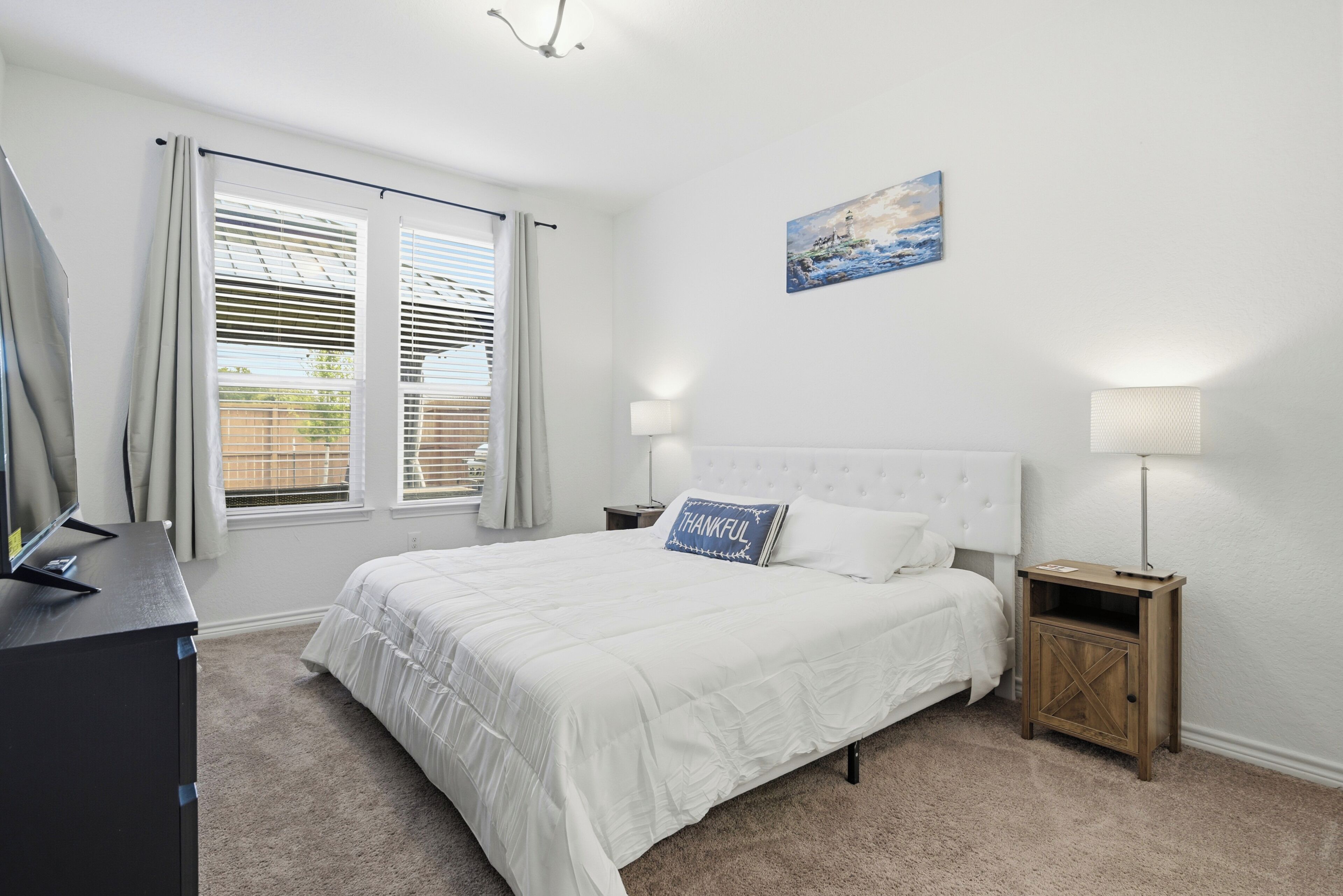 A bedroom with a bed, bedside tables, a lamp, a painting, and a window with curtains.