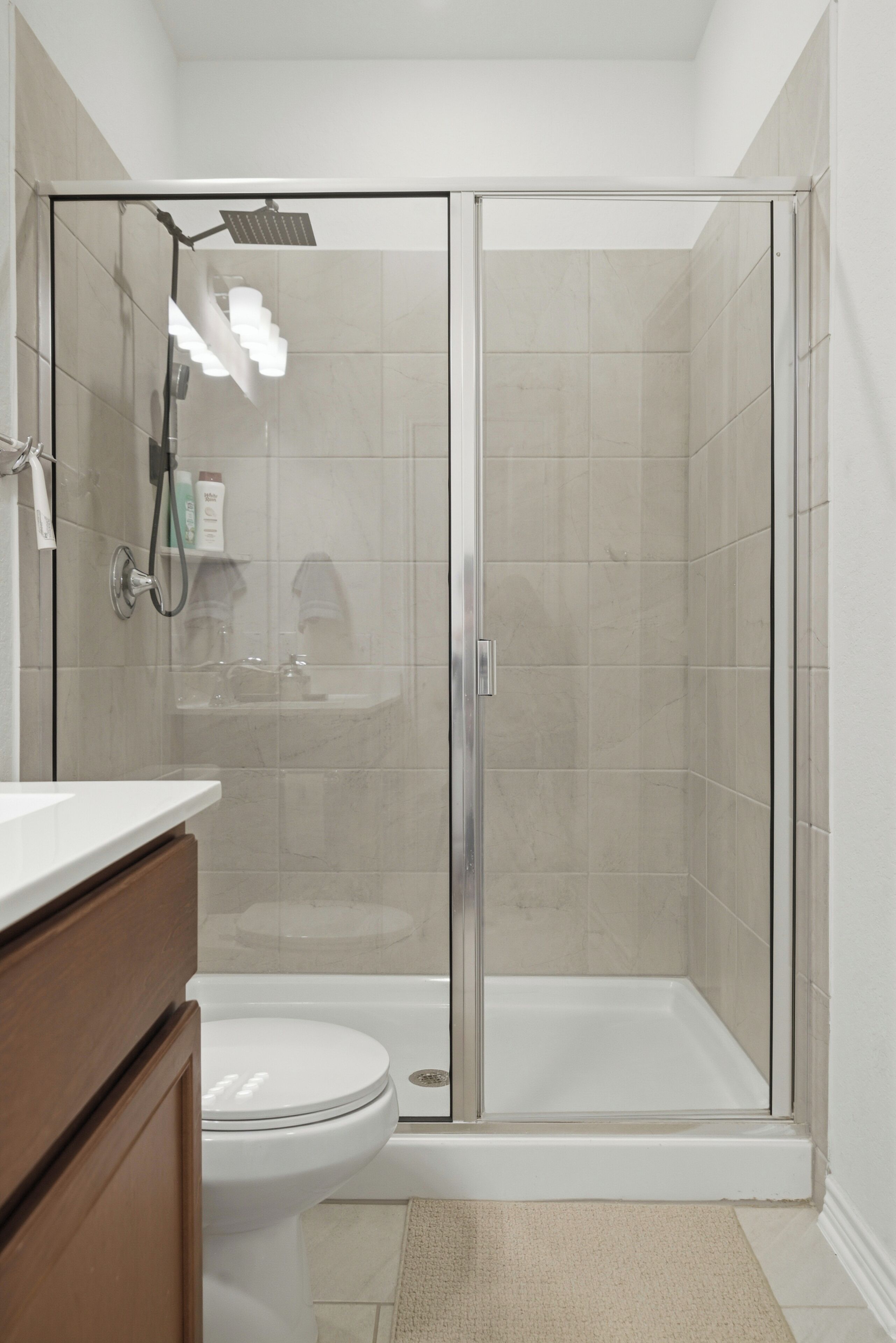 A modern bathroom with a glass-enclosed shower, a white toilet, and a wooden vanity.