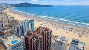 A coastal cityscape with high-rise buildings, a beach with numerous umbrellas, and a clear blue sky. - Beachfront property, 13th floor, heated pool, air conditioning in rooms in Guilhermina, sleeps 8. (Praia Grande)