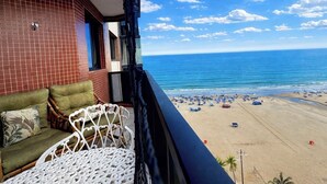 A balcony with a view of the beach, a brick wall, and a white chair. - Beachfront property, 13th floor, heated pool, air conditioning in rooms in Guilhermina, sleeps 8. (Praia Grande)