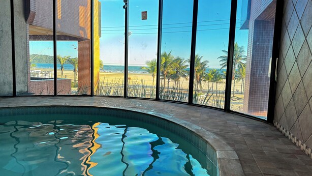 A swimming pool with a view of a beach and palm trees. - Beachfront property, 13th floor, heated pool, air conditioning in rooms in Guilhermina, sleeps 8. (Praia Grande)