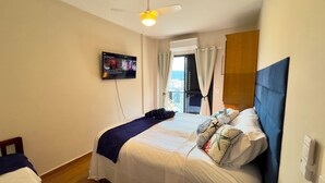 A hotel room with a bed, a ceiling fan, a TV mounted on the wall, and a window with curtains. - Beachfront property, 13th floor, heated pool, air conditioning in rooms in Guilhermina, sleeps 8. (Praia Grande)