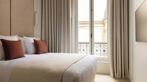 A hotel room with a large bed, curtains, a window with a balcony view, and a wall-mounted light. - Luxury Flat -2br/6p- Madeleine/saint Honore (Paris)