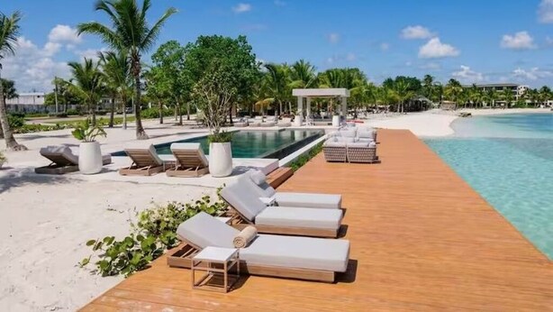 A wooden deck with sun loungers, a pool, and a beach view. - 1BR on P. Lake Vista Lake – Concierge S., Pool & Gym (Punta Cana)