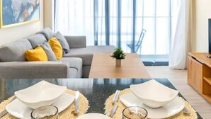A modern living room with a sofa, a coffee table, and a dining area with white plates and cutlery. - 1BR on P. Lake Vista Lake – Concierge S., Pool & Gym (Punta Cana)