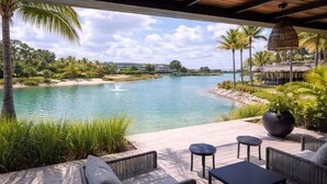 A covered outdoor seating area with a view of a lake and palm trees. - 1BR on P. Lake Vista Lake – Concierge S., Pool & Gym (Punta Cana)