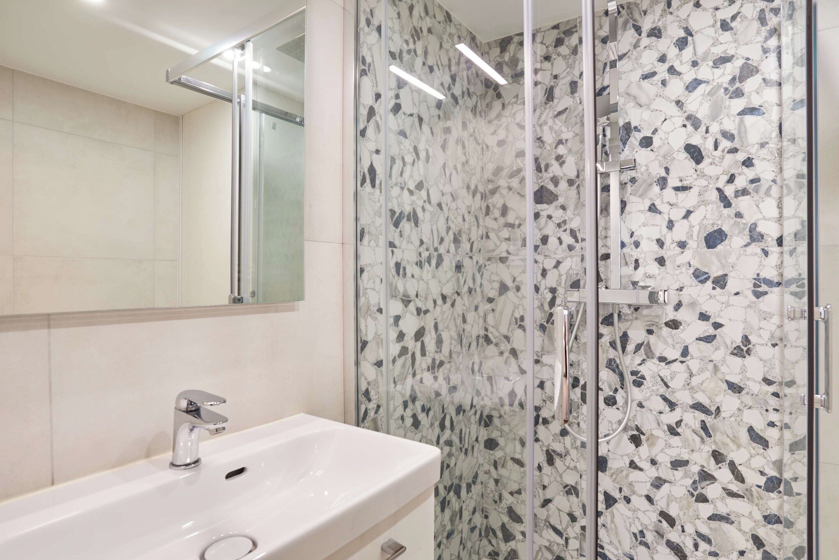 A bathroom with a white sink, a glass shower enclosure, and a mirror.