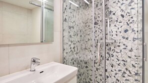 Een badkamer met een wit wastafelmeubel, een douchecabine van glas en een spiegel.