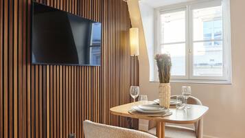 A dining area with a wooden panel wall, a flat-screen TV, a vase with flowers, and a window with blinds.
