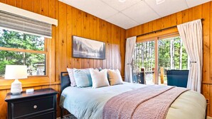 Un dormitorio con paneles de madera, una cama, una mesita de noche y una ventana con vistas a árboles.