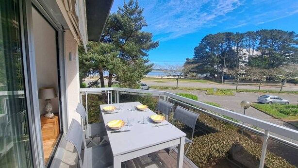 En balkon med et bord dækket til to personer, en lampe og udsigt til en vej og træer.