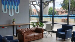Ett modernt loungeområde med en lädersoffa, blå fåtöljer och ett stort fönster som ger utsikt över omgivningen.