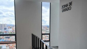 En modern inredning med utsikt över en stadsbild, en trappa med ett svart räcke och en vägg med texten ”TVÄTTZON”.