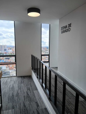 Ein modernes Interieur mit Blick auf die Stadtlandschaft, eine Treppe mit schwarzer Geländer und eine Wand mit der Aufschrift 'ZONA DE LAVADO'.