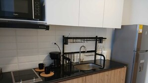 Ett modernt kök med mikrovågsugn, kaffebryggare, diskho med en svart blandare och ett kylskåp i rostfritt stål.