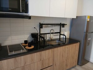Eine moderne Küche mit Mikrowelle, Kaffeemaschine, Spüle mit schwarzem Wasserhahn und einem Edelstahl-Kühlschrank.