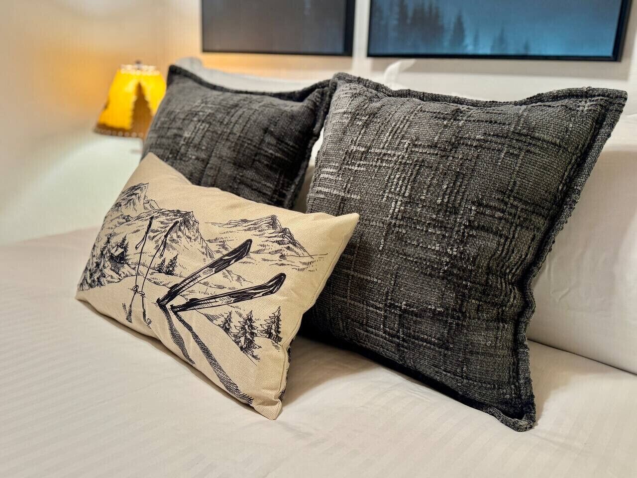 A bed with two pillows, one with a mountain design and the other plain.
