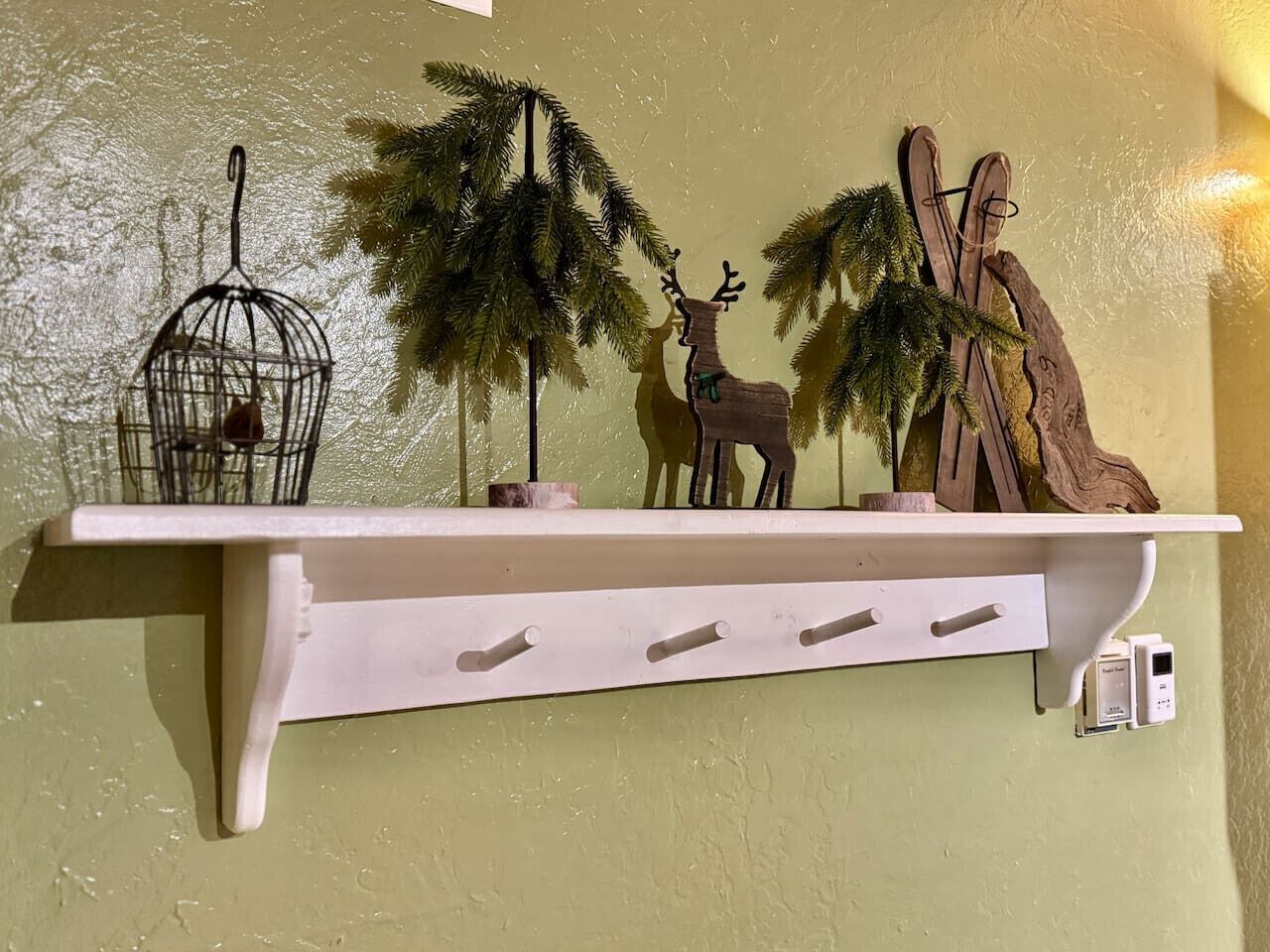A white wall-mounted shelf with a birdcage, a wooden deer, and a pair of skis.