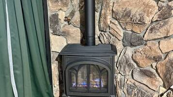 En vedeldad kamin med skorsten, placerad framför en stenmur, och en grön gardin syns delvis.
