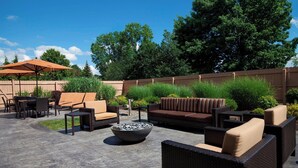 Eine Außenpatio-Terrasse mit Korbmöbeln, einer Stein-Feuerstelle und einem Holzzaun.