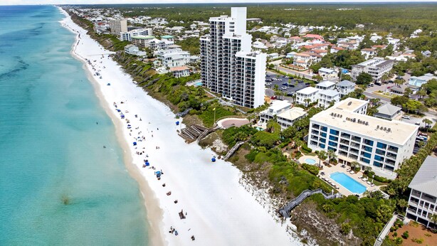 Vista aérea de una zona costera con playa, un hotel grande de varios pisos y edificios residenciales circundantes.