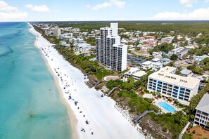 Ein Luftbild einer Küstenregion mit Strand, einem großen Mehrstöckigen Hotel und umliegenden Wohngebäuden.