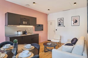 A modern kitchen with dark cabinets and a white countertop, a dining area with a round table and chairs, and a living area with a sofa and a coffee table. - Charming Apartment Beaubourg - Le Marais (Paris)