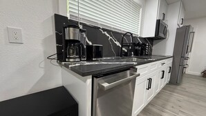 A modern kitchen with a black countertop, stainless steel appliances, and white cabinets. - Modern Luxury Studio Cozy Retreat (Zephyrhills)