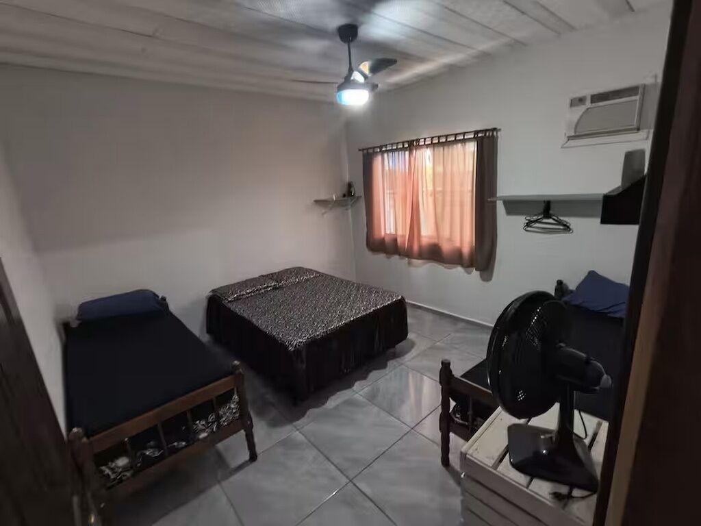 A room with two beds, a ceiling fan, a window with curtains, a desk with a chair, and a wall-mounted air conditioner.