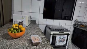 Une cuisine avec des murs recouverts de carreaux blancs, un plan de travail en granit, une cuisinière à gaz et une fenêtre.